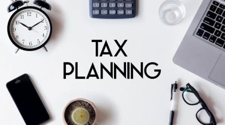 Tax Planning words written on white table with clock, smartphone, calculator, pen, cactus, glass and laptop